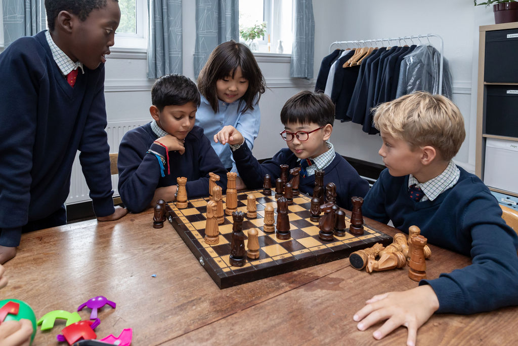 A group of boys and girls at Horris Hill school gather around a chess board