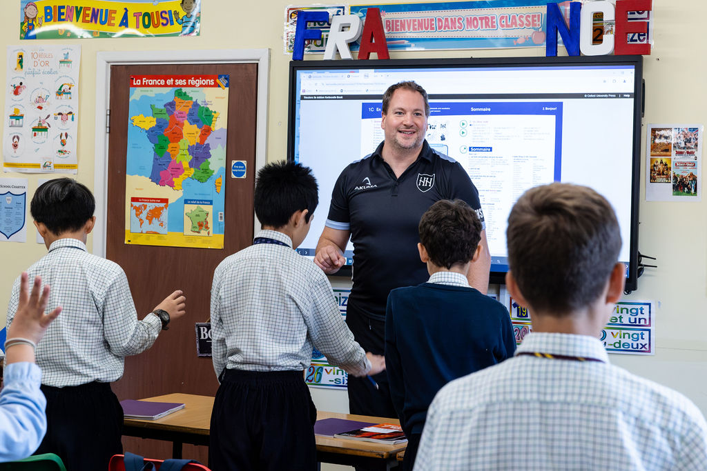 A teacher stands at the front of the classroom, speaking to pupils